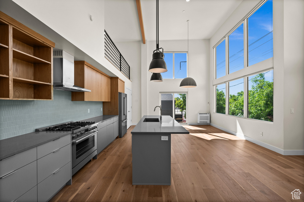 Kitchen featuring wall chimney exhaust hood, appliances with stainless steel finishes, a sink, modern cabinets, and baseboards