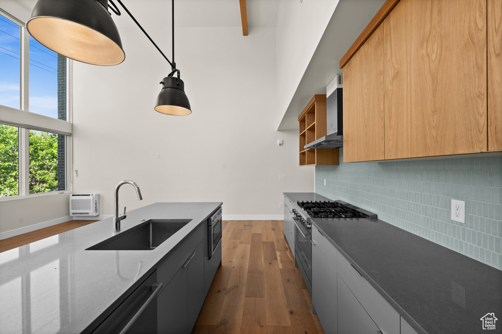 Kitchen with wall chimney range hood, a sink, appliances with stainless steel finishes, a high ceiling, and wood finished floors
