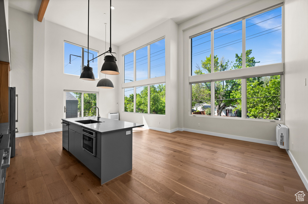 Kitchen featuring a sink, an island with sink, a high ceiling, dark wood finished floors, and baseboards