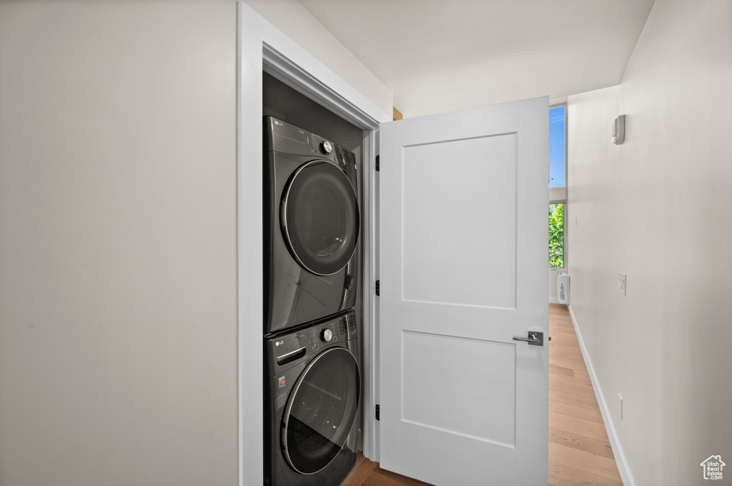 Laundry room featuring stacked washing machine and dryer, wood finished floors, and baseboards
