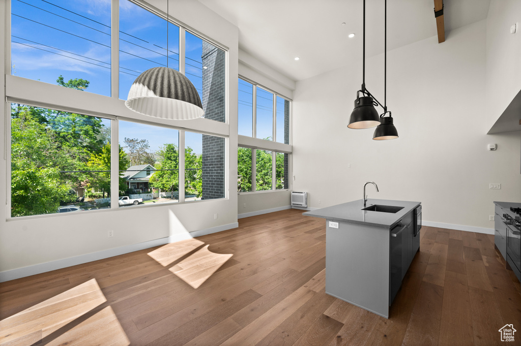 Kitchen with a sink, a towering ceiling, baseboards, a center island with sink, and dark wood-type flooring