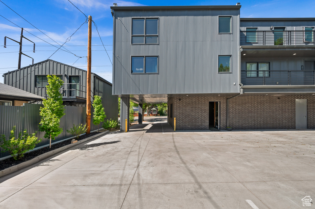 Back of house featuring a carport, driveway, brick siding, and fence