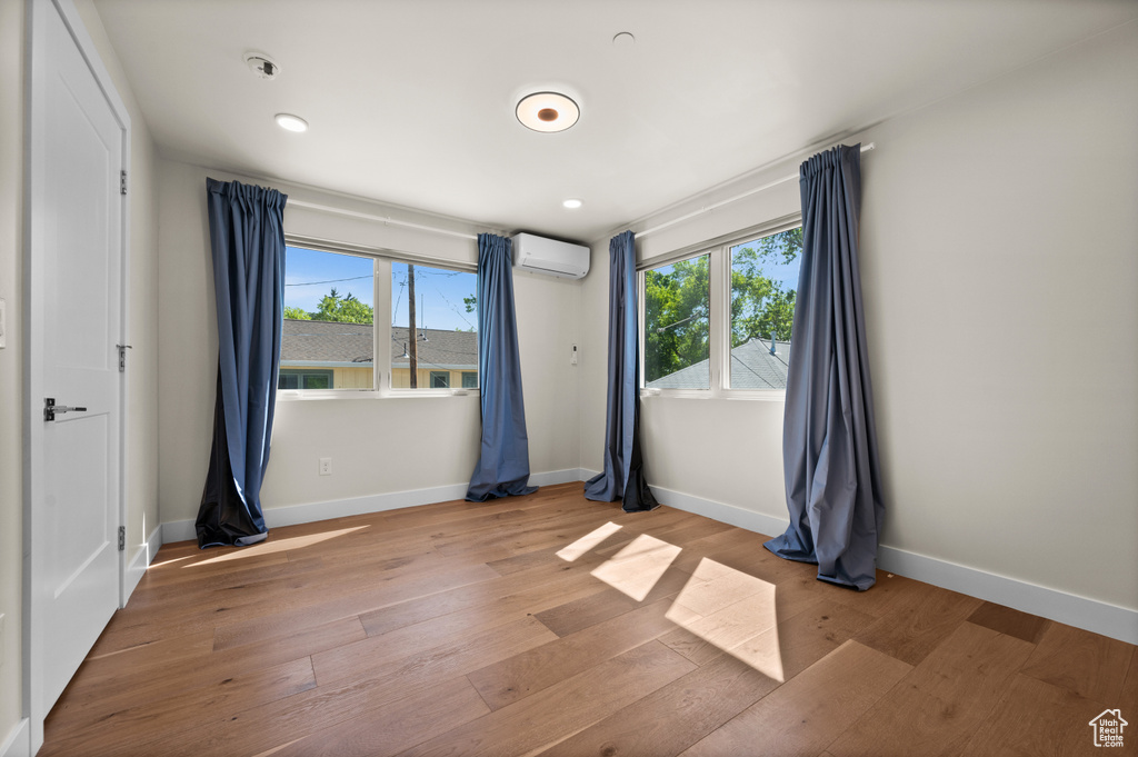 Unfurnished bedroom featuring a wall mounted AC, light wood-style flooring, and baseboards