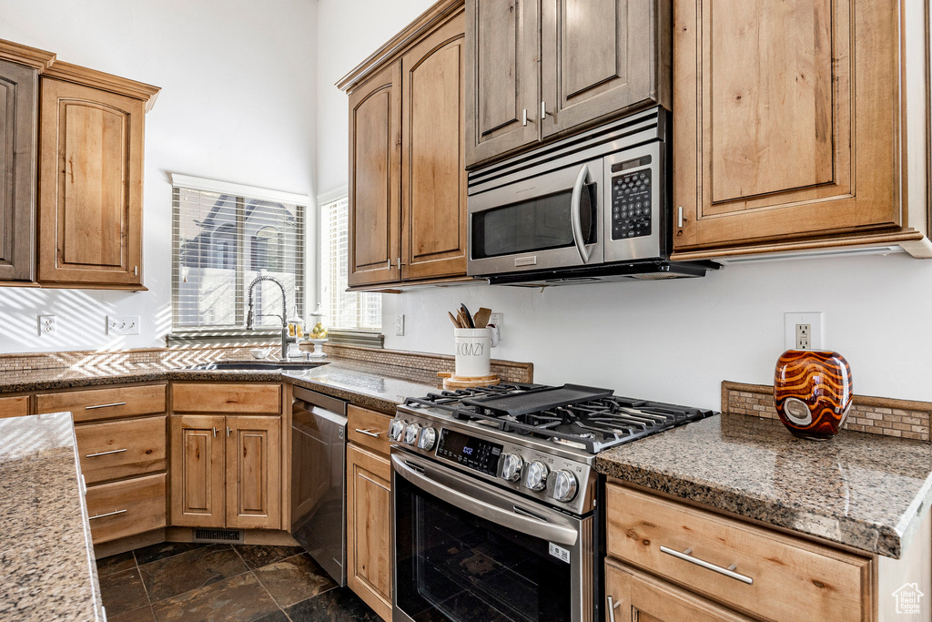 Kitchen featuring stainless steel appliances, a sink, dark stone finish floors, and light stone counters