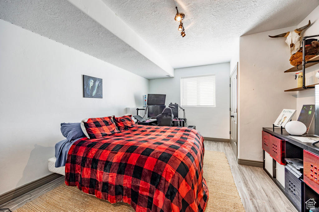 Bedroom with light wood finished floors, a textured ceiling, and baseboards