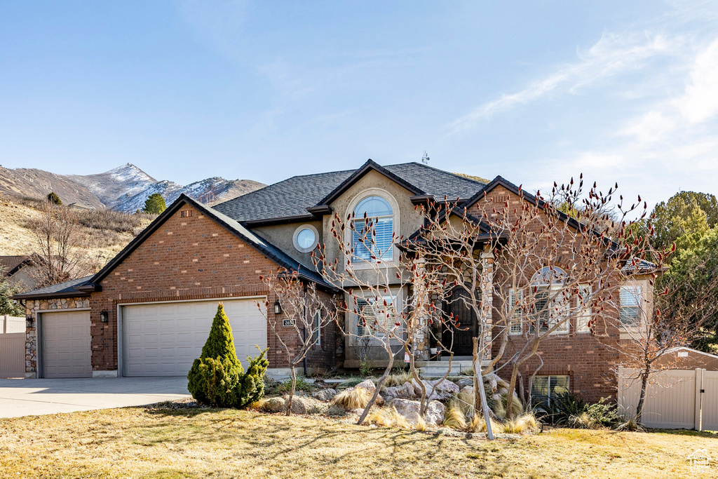 View of front of property with a garage, concrete driveway, fence, brick siding, and a mountain view