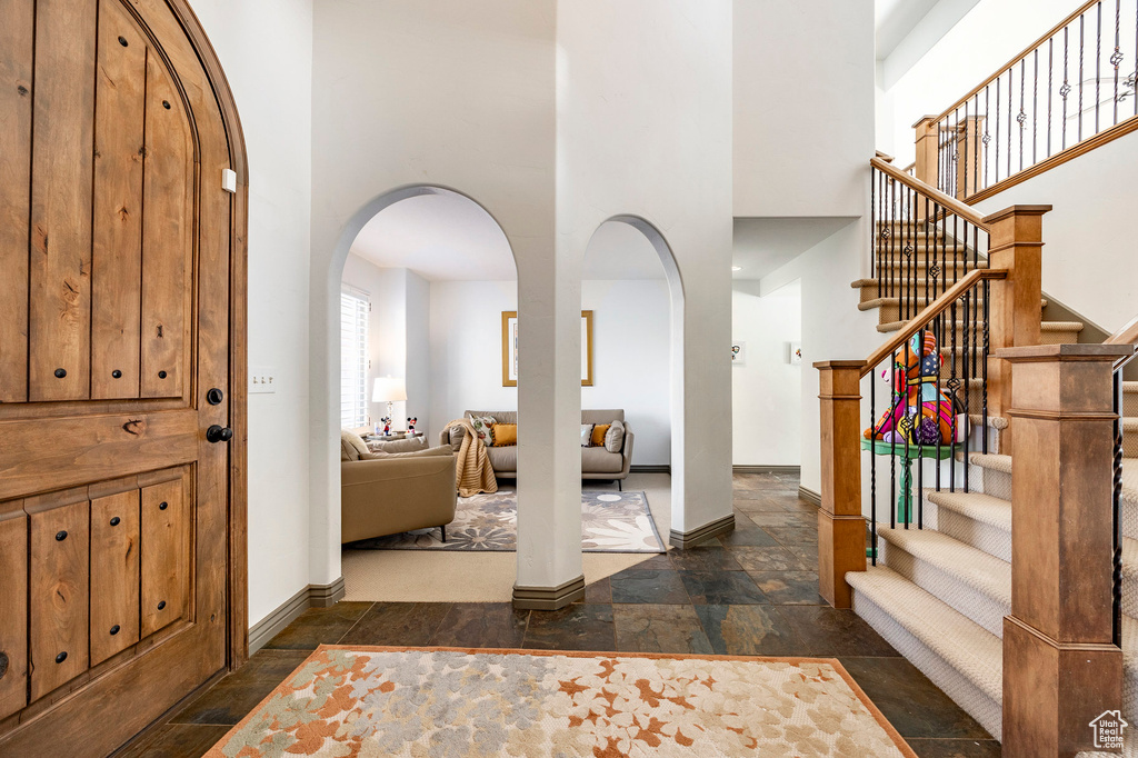 Entryway with arched walkways, a high ceiling, baseboards, stone tile floors, and stairway