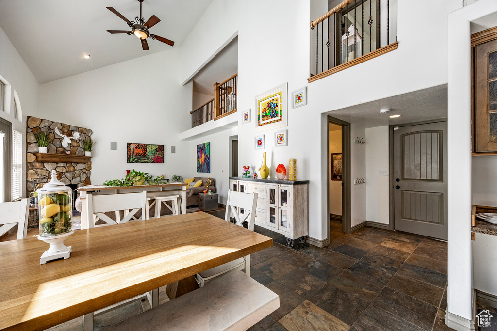 Dining space with high vaulted ceiling, baseboards, a ceiling fan, and stone tile flooring