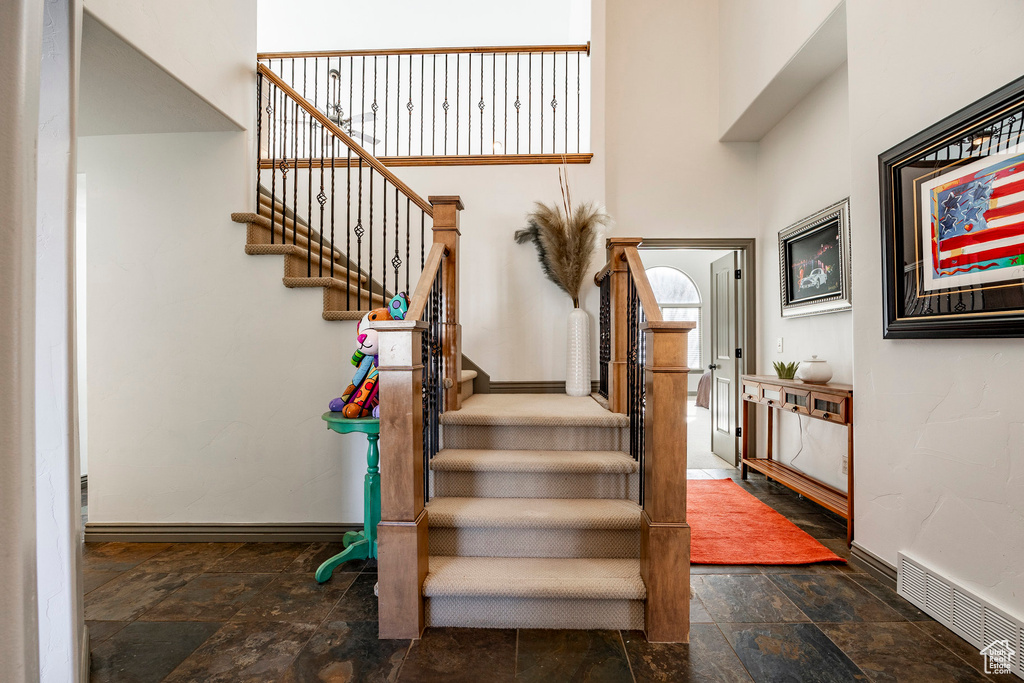 Stairs featuring stone tile flooring, baseboards, and a towering ceiling