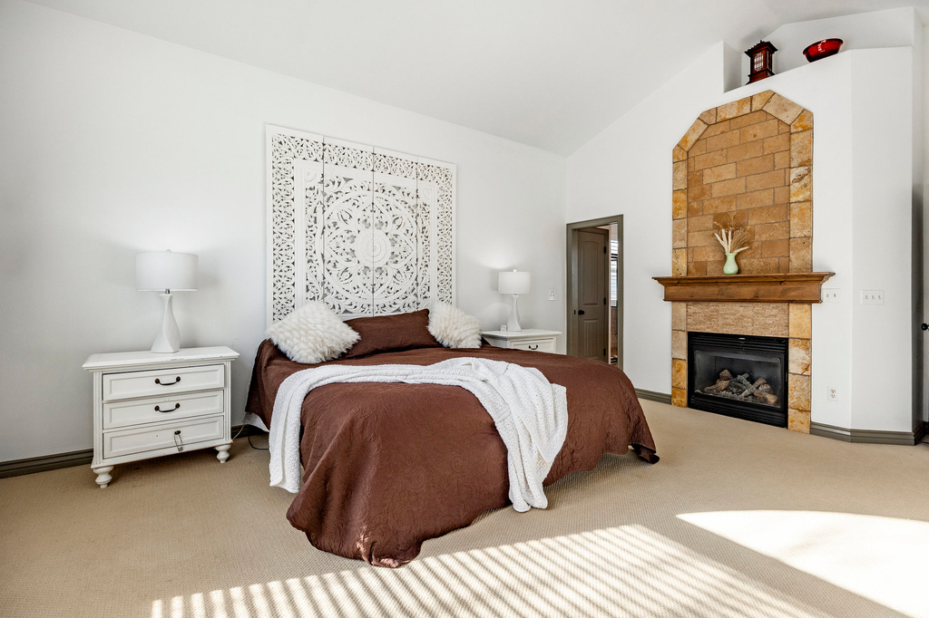 Carpeted bedroom with a tiled fireplace, baseboards, and high vaulted ceiling