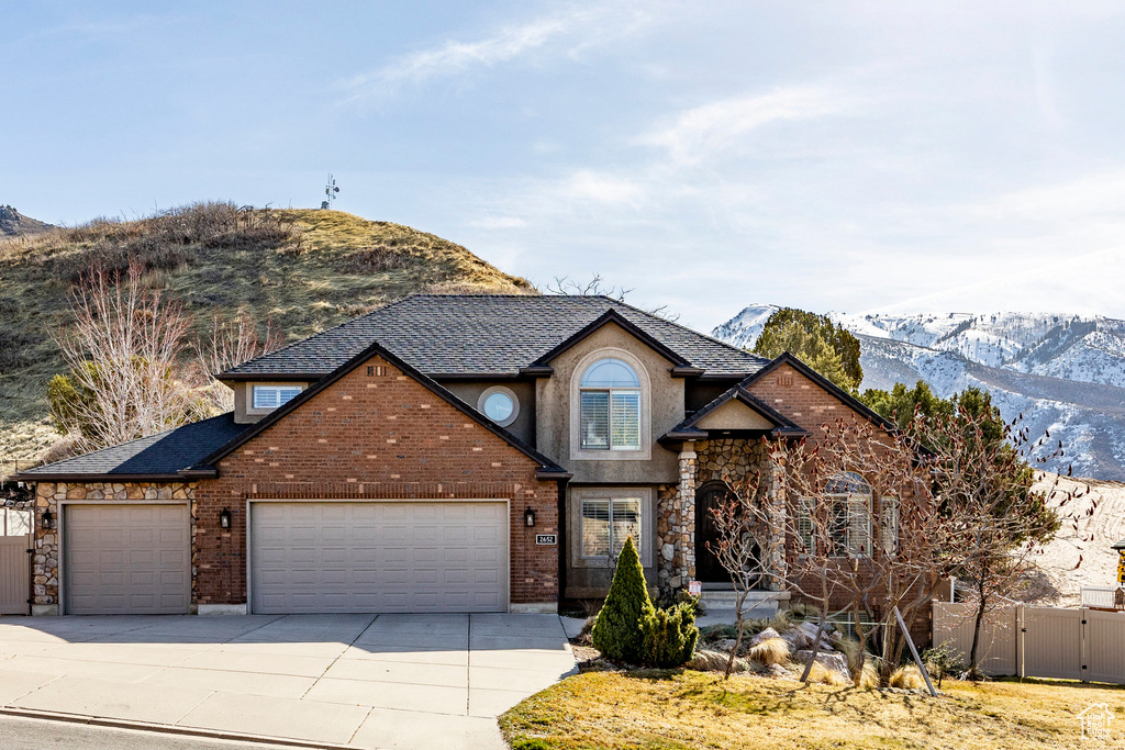 Traditional home featuring an attached garage, a mountain view, driveway, fence, and a gate