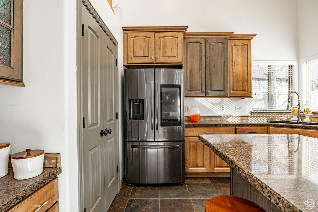 Kitchen featuring stainless steel fridge with ice dispenser, a sink, dark stone finish floors, dark stone countertops, and brown cabinetry