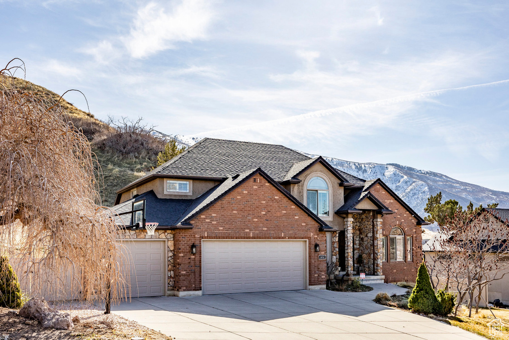 Traditional-style home with concrete driveway, a garage, brick siding, a mountain view, and roof with shingles