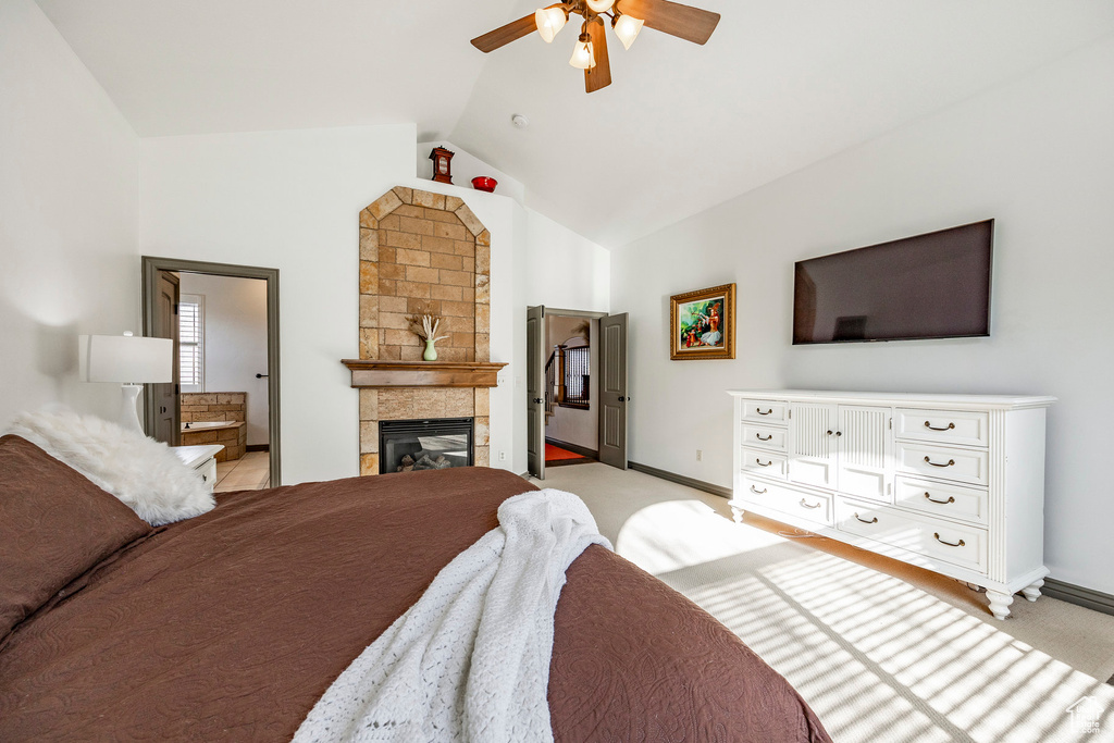 Bedroom featuring vaulted ceiling, baseboards, a tiled fireplace, light carpet, and ceiling fan