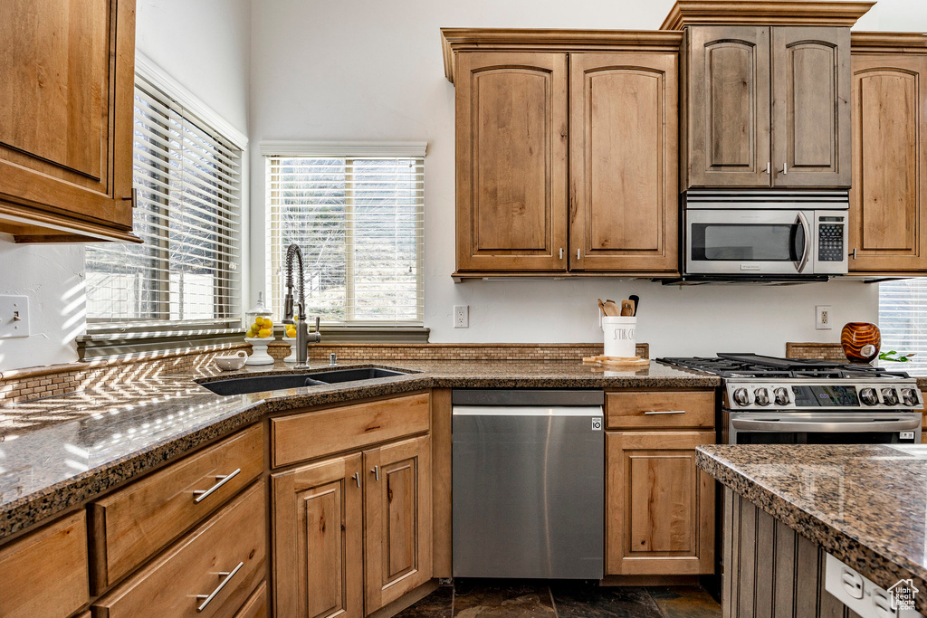 Kitchen with appliances with stainless steel finishes, a sink, plenty of natural light, and dark stone counters