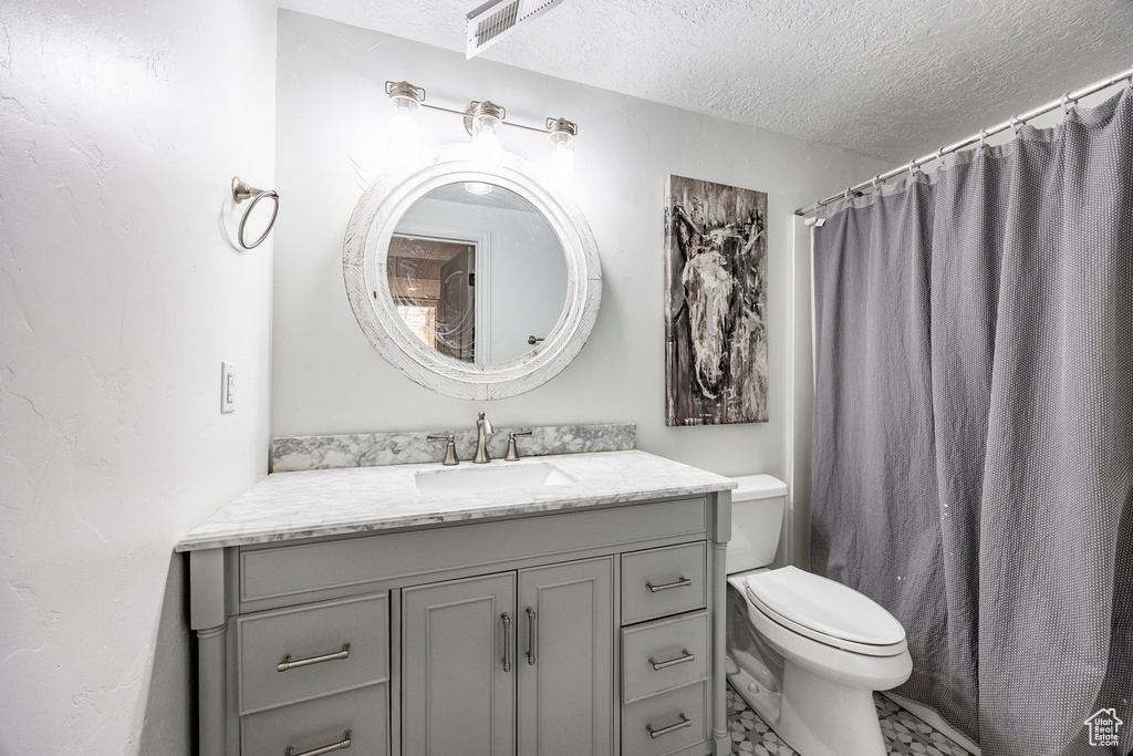Bathroom featuring a textured ceiling, toilet, vanity, and curtained shower
