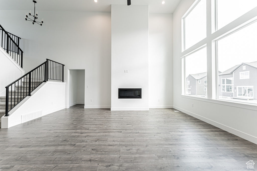 Unfurnished living room with a high ceiling, stairway, a glass covered fireplace, wood finished floors, and a chandelier