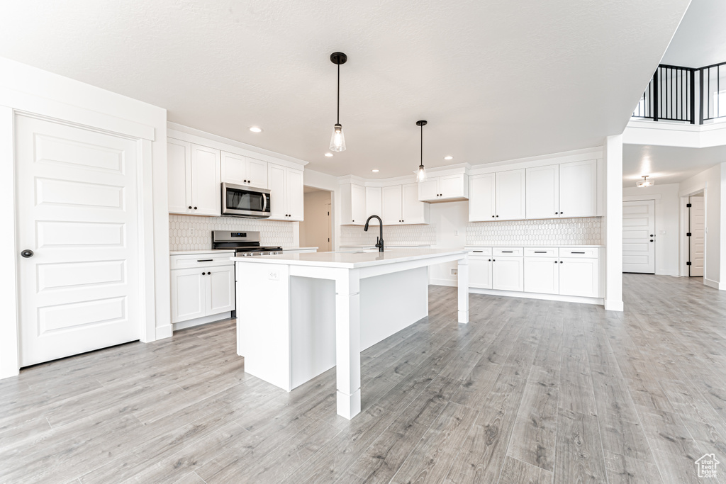 Kitchen with stainless steel microwave, backsplash, light countertops, light wood finished floors, and recessed lighting