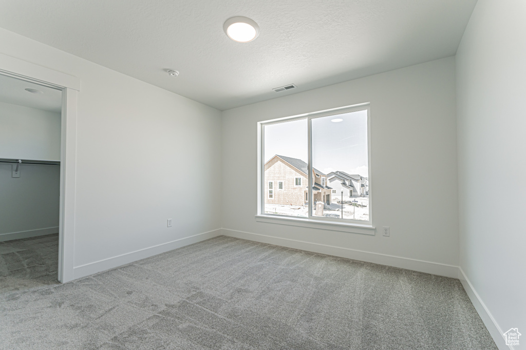 Unfurnished bedroom featuring carpet floors, a walk in closet, a closet, and a textured ceiling
