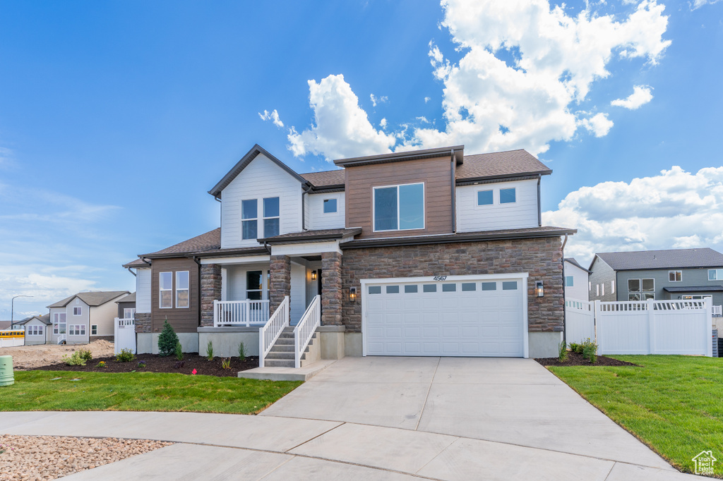 View of front of home featuring covered porch, a garage, concrete driveway, and stone siding