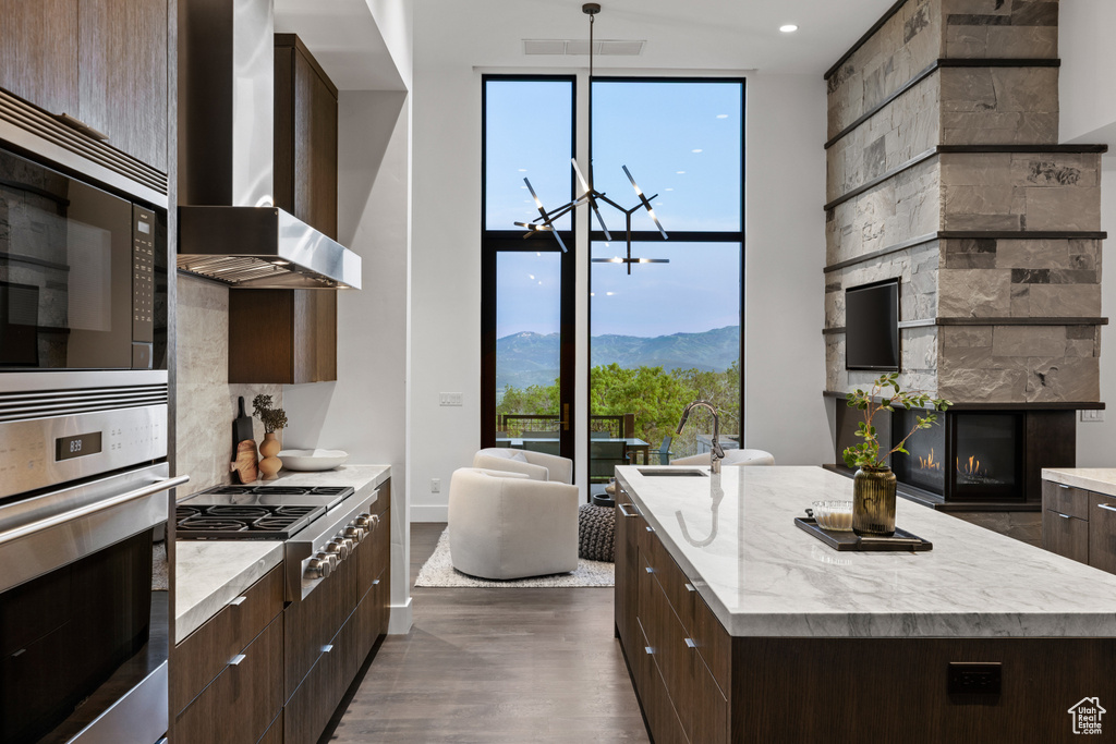 Kitchen with stainless steel appliances, wall chimney range hood, modern cabinets, a wall of windows, and plenty of natural light