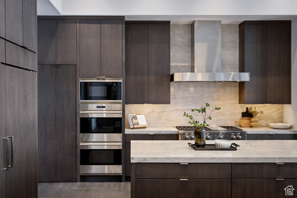 Kitchen featuring wall chimney exhaust hood, appliances with stainless steel finishes, dark brown cabinets, and modern cabinets