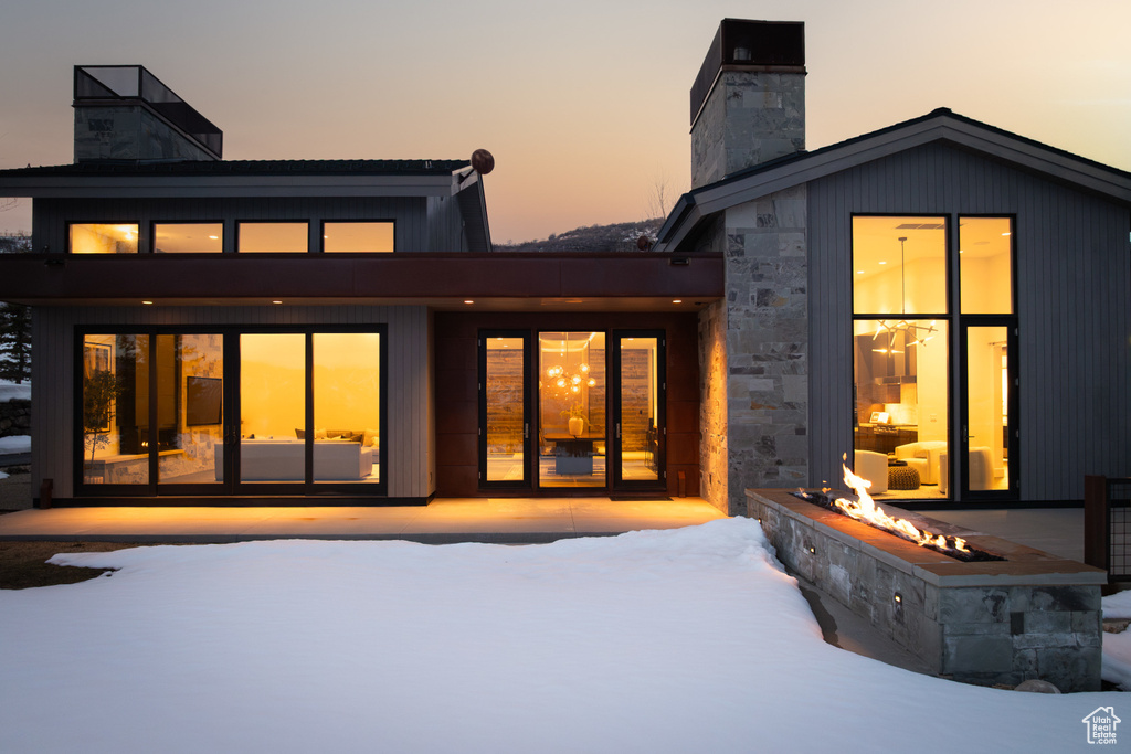 Snow covered property with a chimney and stone siding