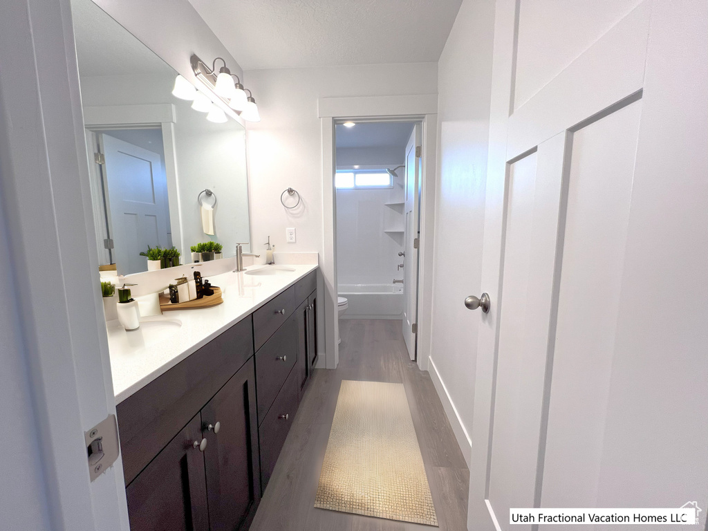 Bathroom featuring wood finished floors, double vanity,  shower combination, a sink, and toilet
