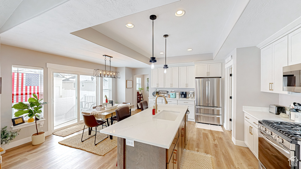 Kitchen featuring a sink, a tray ceiling, light wood-style floors, appliances with stainless steel finishes, and light countertops