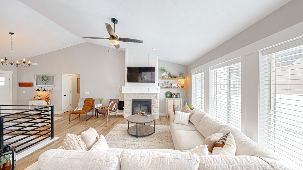 Living room featuring a glass covered fireplace, lofted ceiling, ceiling fan with notable chandelier, and light wood-type flooring