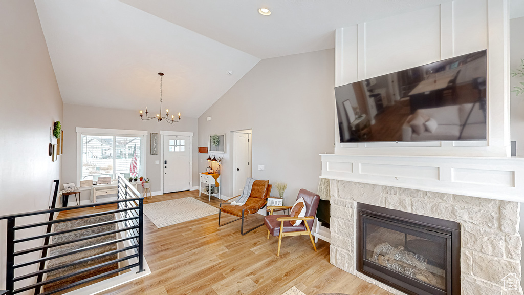 Living room with light wood finished floors, a stone fireplace, recessed lighting, a notable chandelier, and high vaulted ceiling