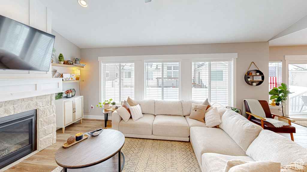 Living room with light wood-type flooring, plenty of natural light, a glass covered fireplace, and vaulted ceiling