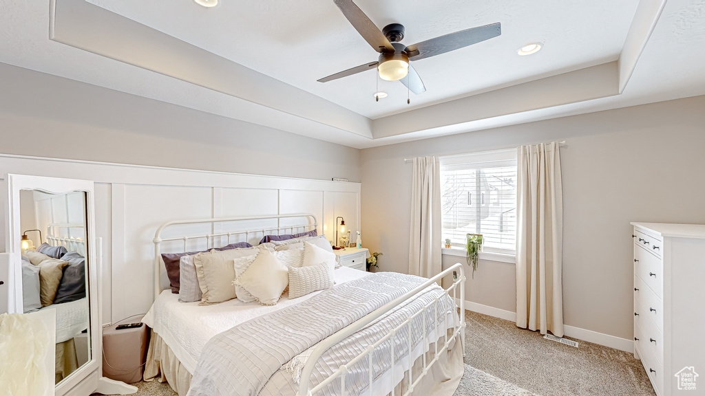 Bedroom featuring visible vents, baseboards, light colored carpet, a tray ceiling, and a ceiling fan