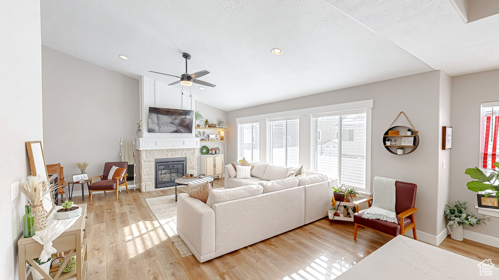 Living area with baseboards, ceiling fan, light wood-type flooring, vaulted ceiling, and a stone fireplace