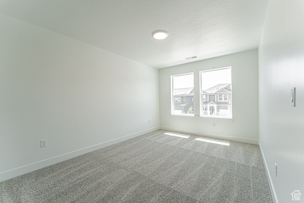 Empty room with baseboards, carpet, and a textured ceiling