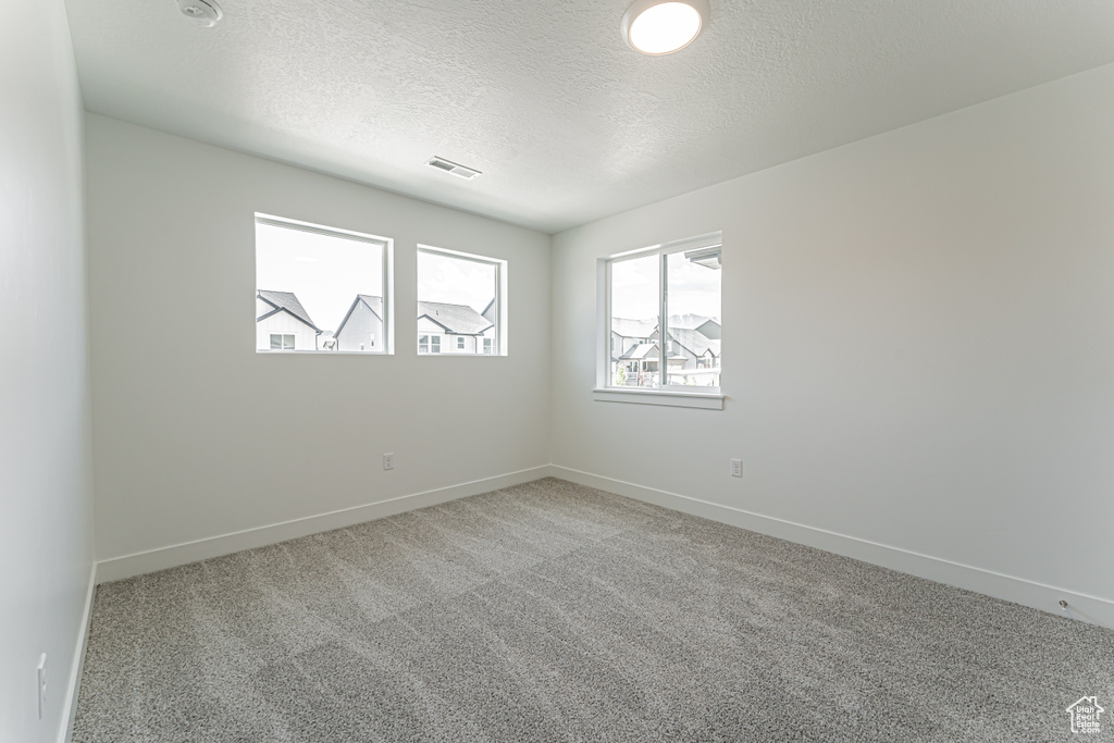 Spare room featuring a textured ceiling, carpet flooring, and baseboards