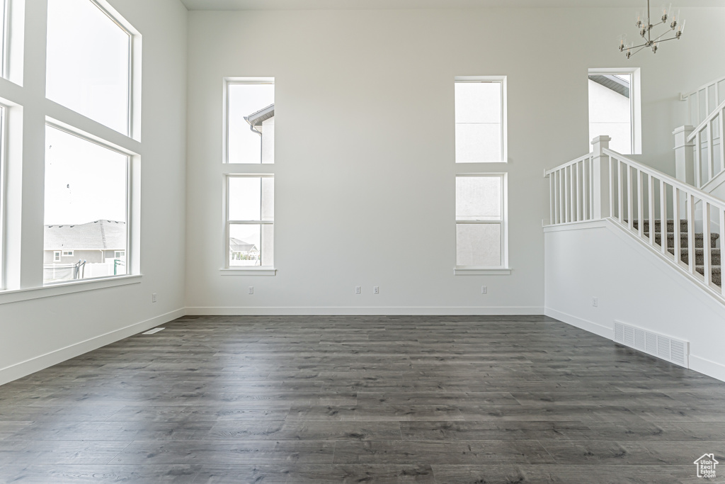Empty room featuring stairs, plenty of natural light, a chandelier, and dark wood finished floors