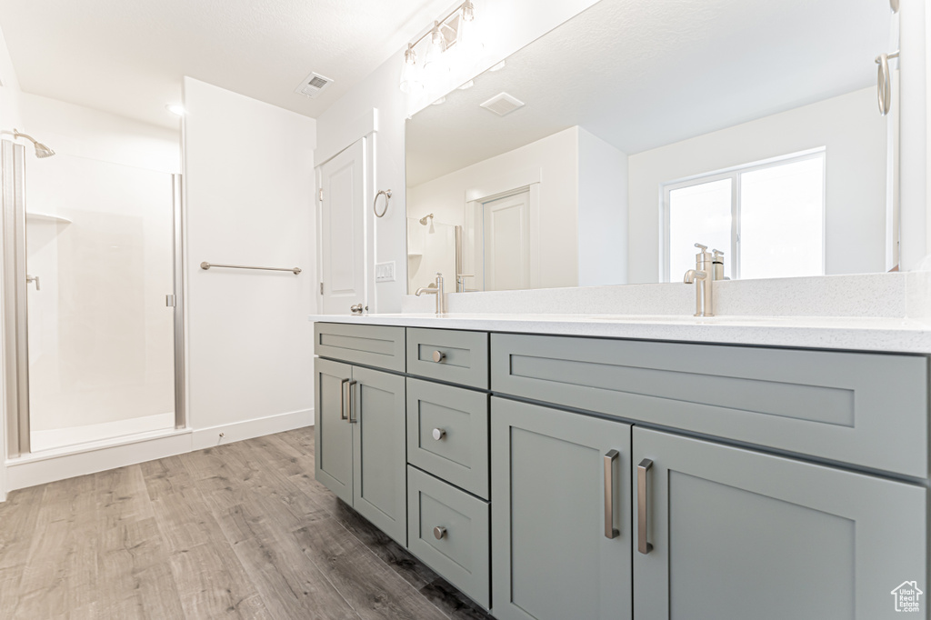 Bathroom with double vanity, wood finished floors, a shower stall, and baseboards