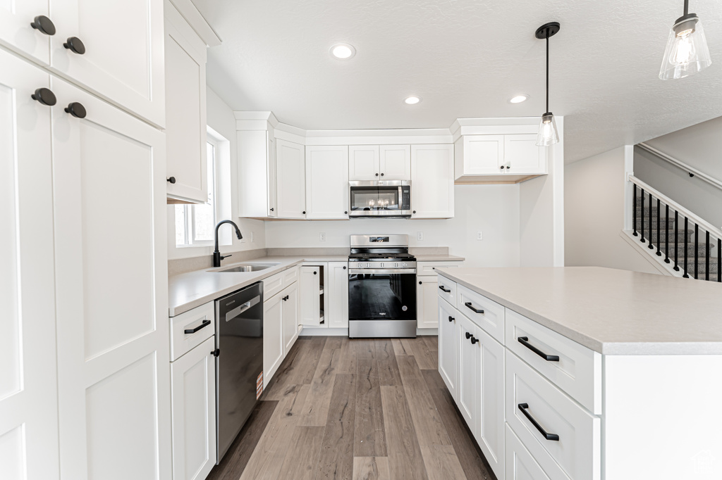 Kitchen featuring appliances with stainless steel finishes, light wood finished floors, recessed lighting, light countertops, and decorative light fixtures