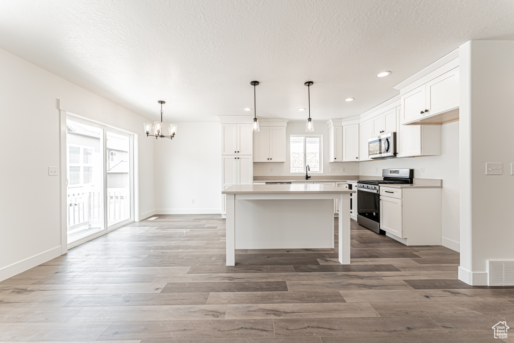Kitchen featuring appliances with stainless steel finishes, a chandelier, recessed lighting, white cabinetry, and a center island