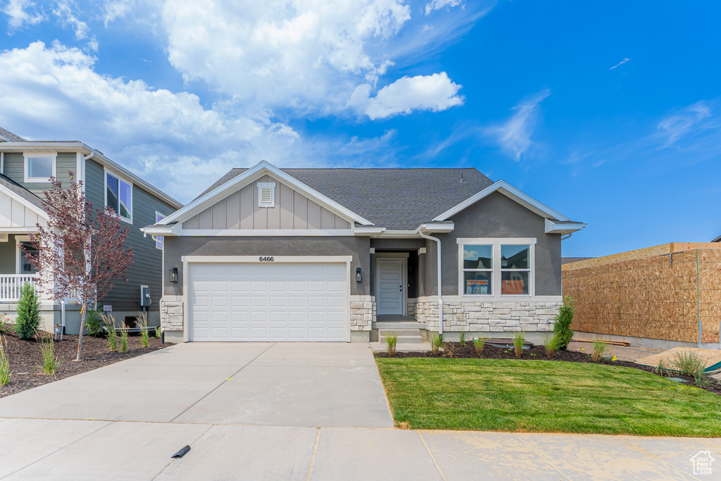 Craftsman-style house featuring stone siding, driveway, an attached garage, board and batten siding, and stucco siding