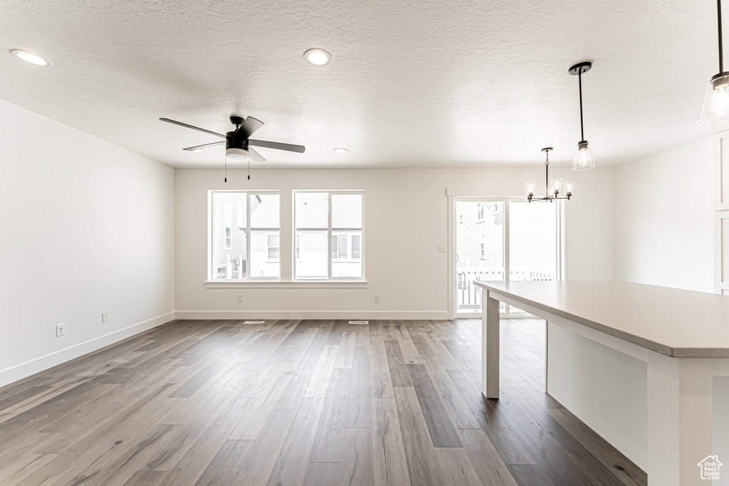 Unfurnished living room featuring a chandelier, ceiling fan, dark wood-style floors, a textured ceiling, and recessed lighting