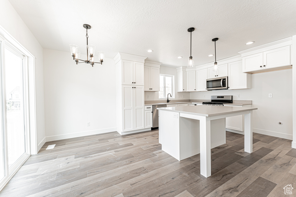 Kitchen with appliances with stainless steel finishes, a chandelier, light countertops, white cabinetry, and a kitchen island