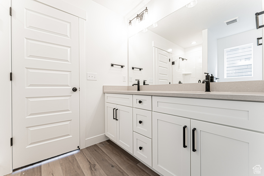Full bathroom featuring double vanity, wood finished floors, and a shower