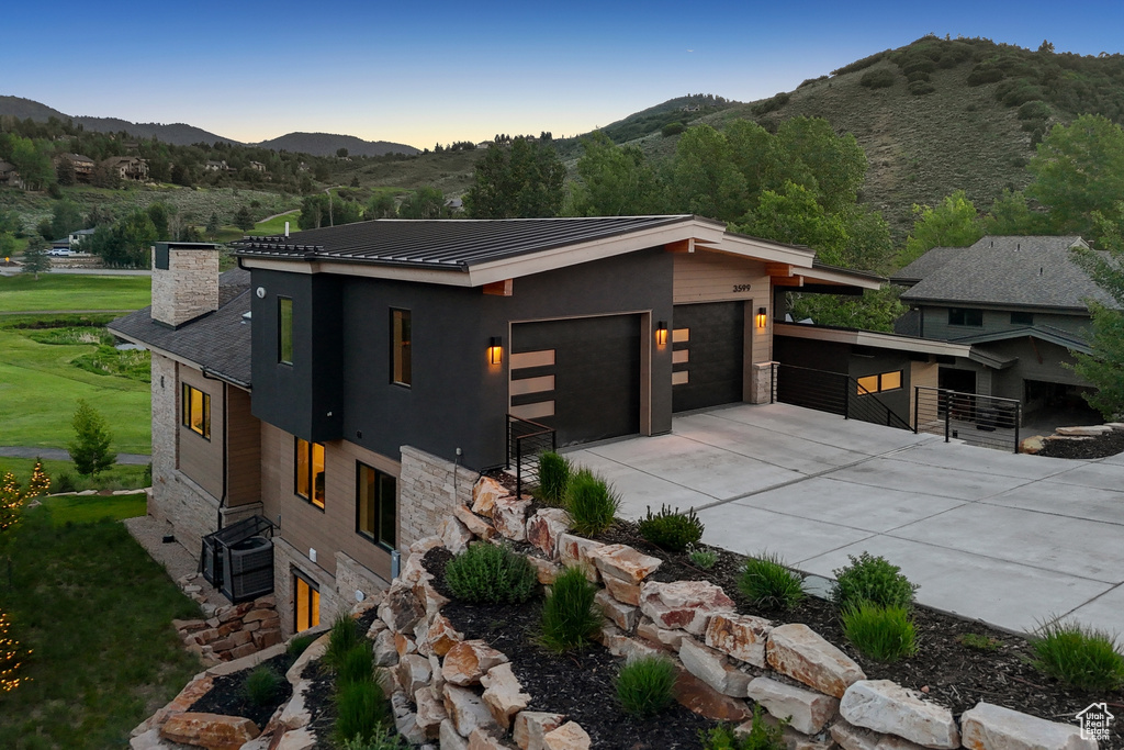 Contemporary house with stone siding, a mountain view, a chimney, driveway, and a metal roof