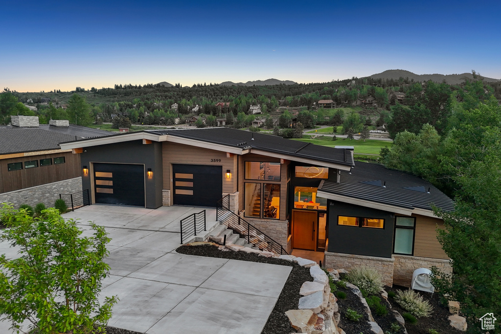 Modern home with stone siding, a garage, concrete driveway, and a mountain view