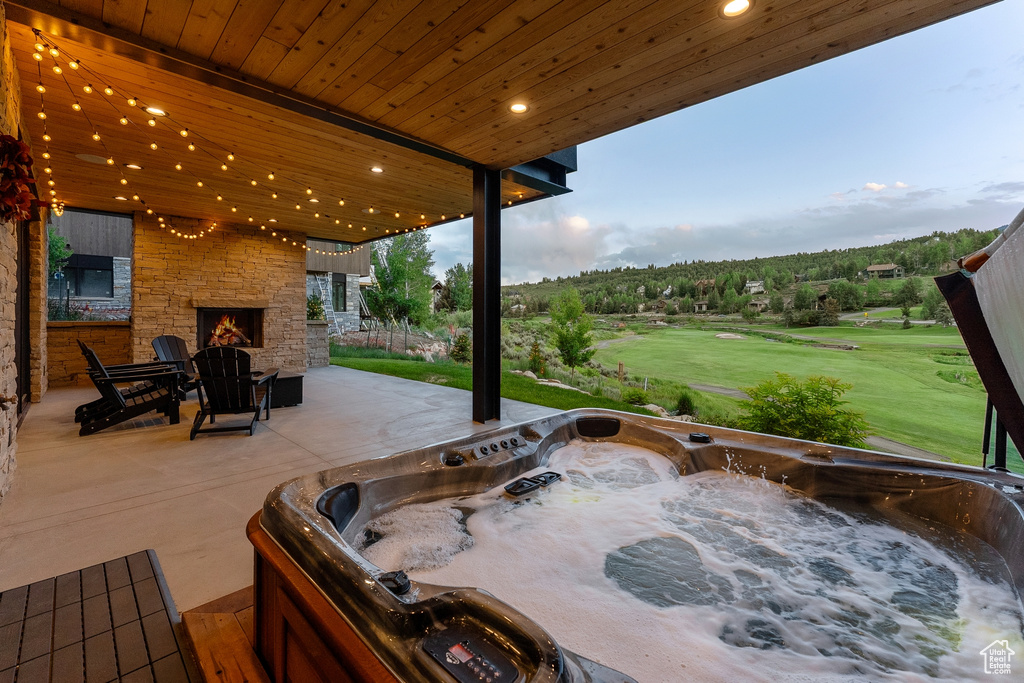 View of patio featuring an outdoor stone fireplace, a hot tub, and golf course view