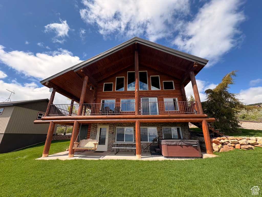 Rear view of property featuring a hot tub, log exterior, a patio area, stone siding, and a balcony