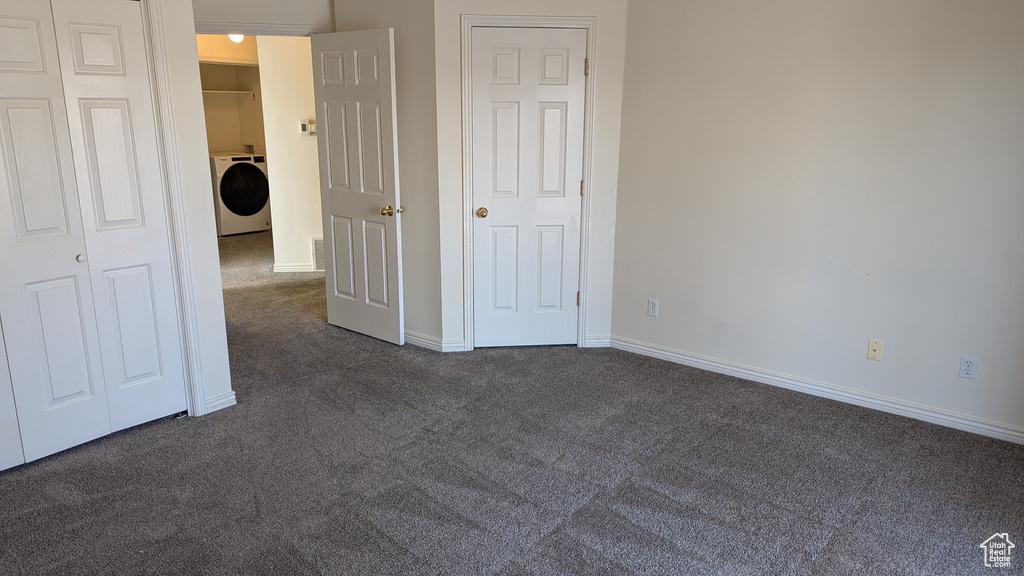 Unfurnished bedroom featuring washer / dryer, baseboards, dark colored carpet, and a closet