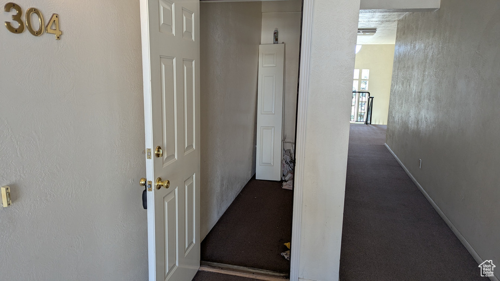 Corridor featuring baseboards, dark carpet, and a textured wall